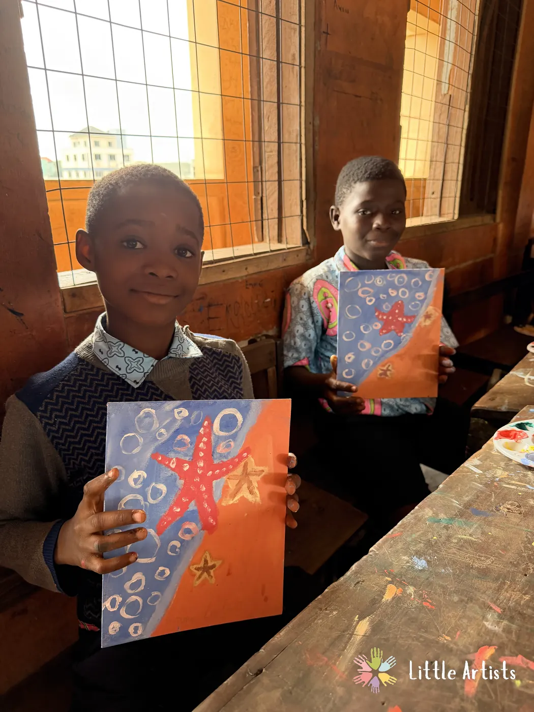 Two students holding their starfish paintings in the window light